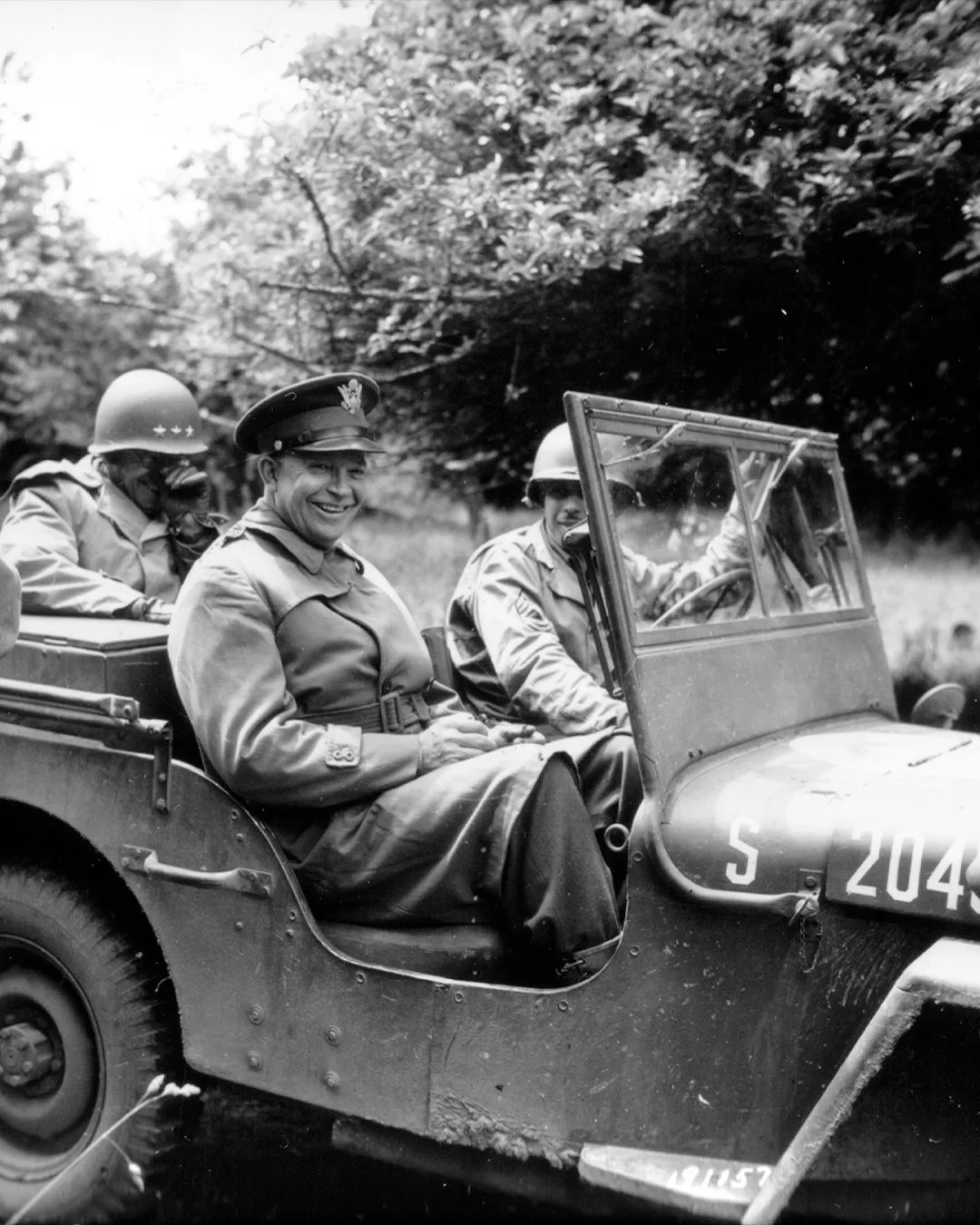 Black and white photo of three soldiers in a military jeep, one smiling in the front passenger seat.