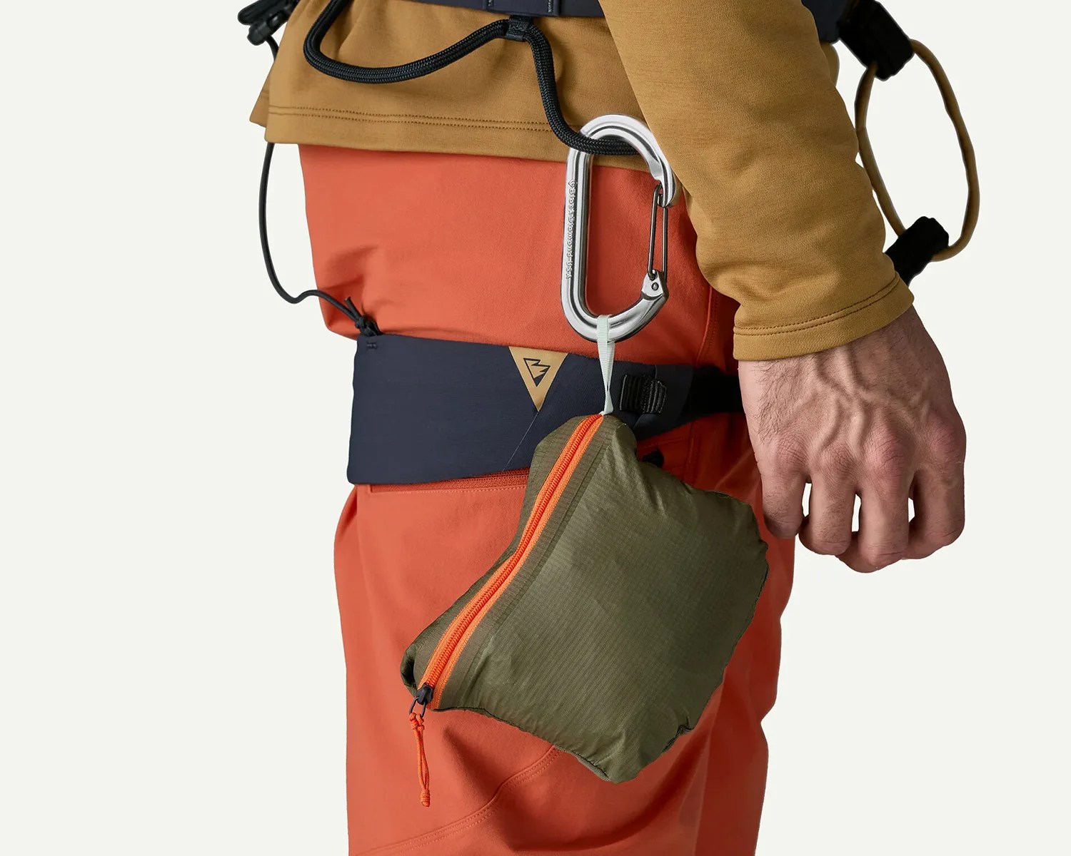 Silver carabiner clipped to a black belt loop on orange pants, holding a small olive green pouch with an orange zipper.