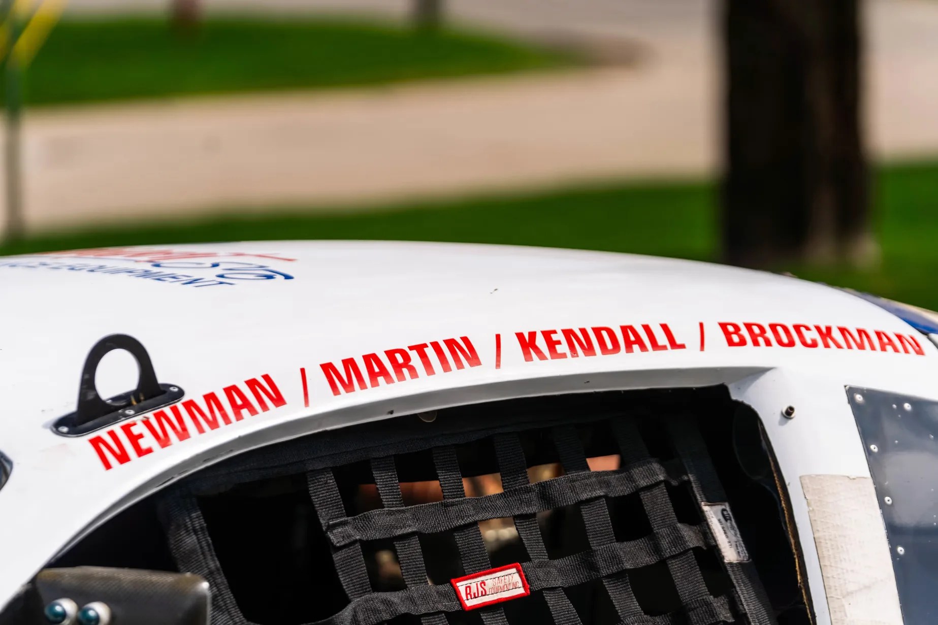 White race car roof with red names "NEWMAN / MARTIN / KENDALL / BROCKMAN" above a black safety net window.