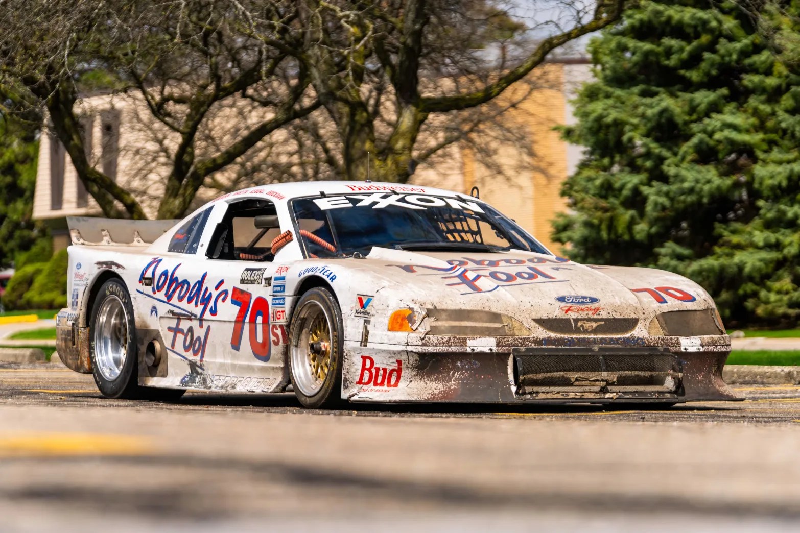 White Ford Mustang race car with "Nobody's Fool" and number 70 decals, showing dirt and wear.