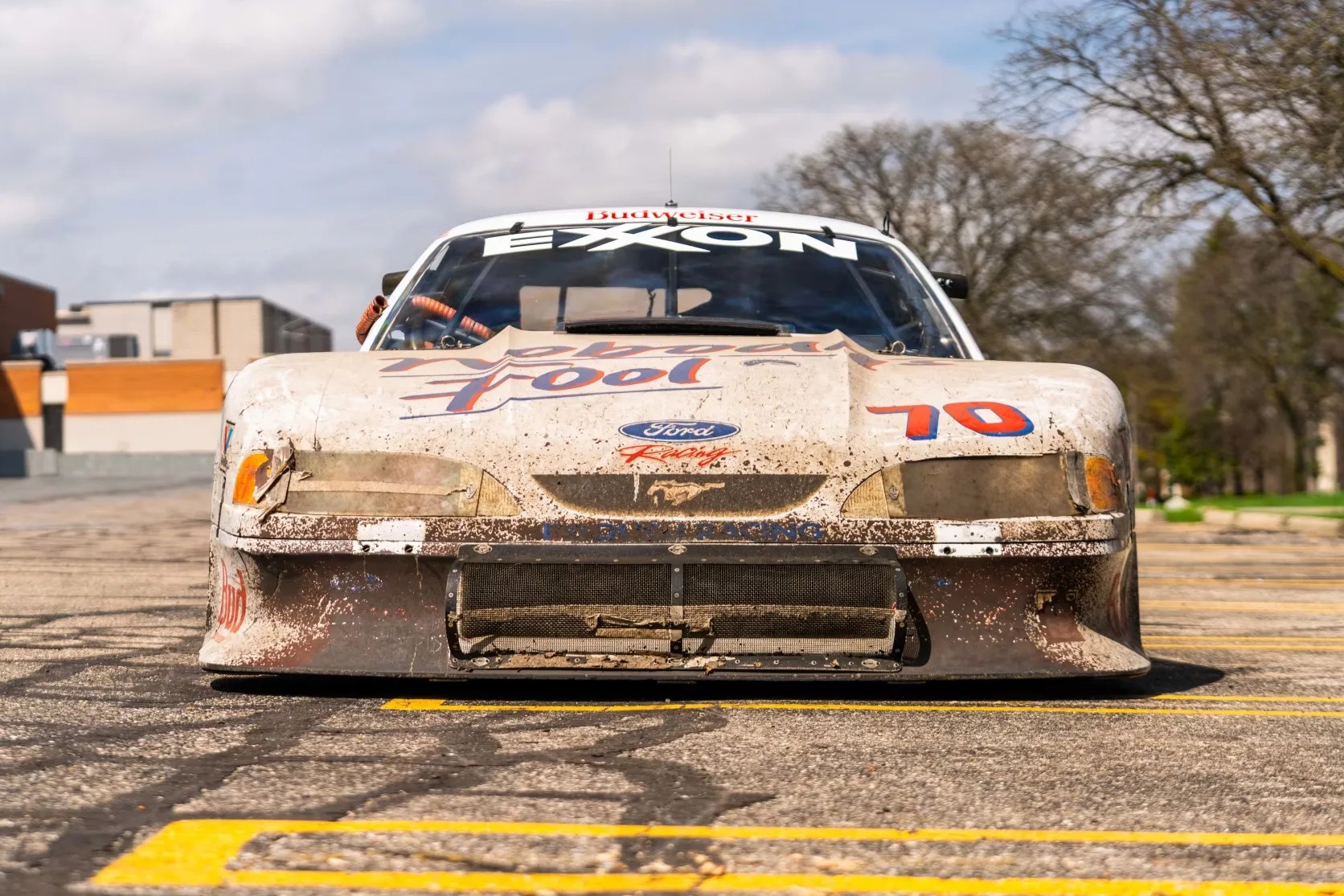 Front view of a dirty white Ford Mustang race car with "Budweiser" and "Exxon" decals and the number 10 on the hood.