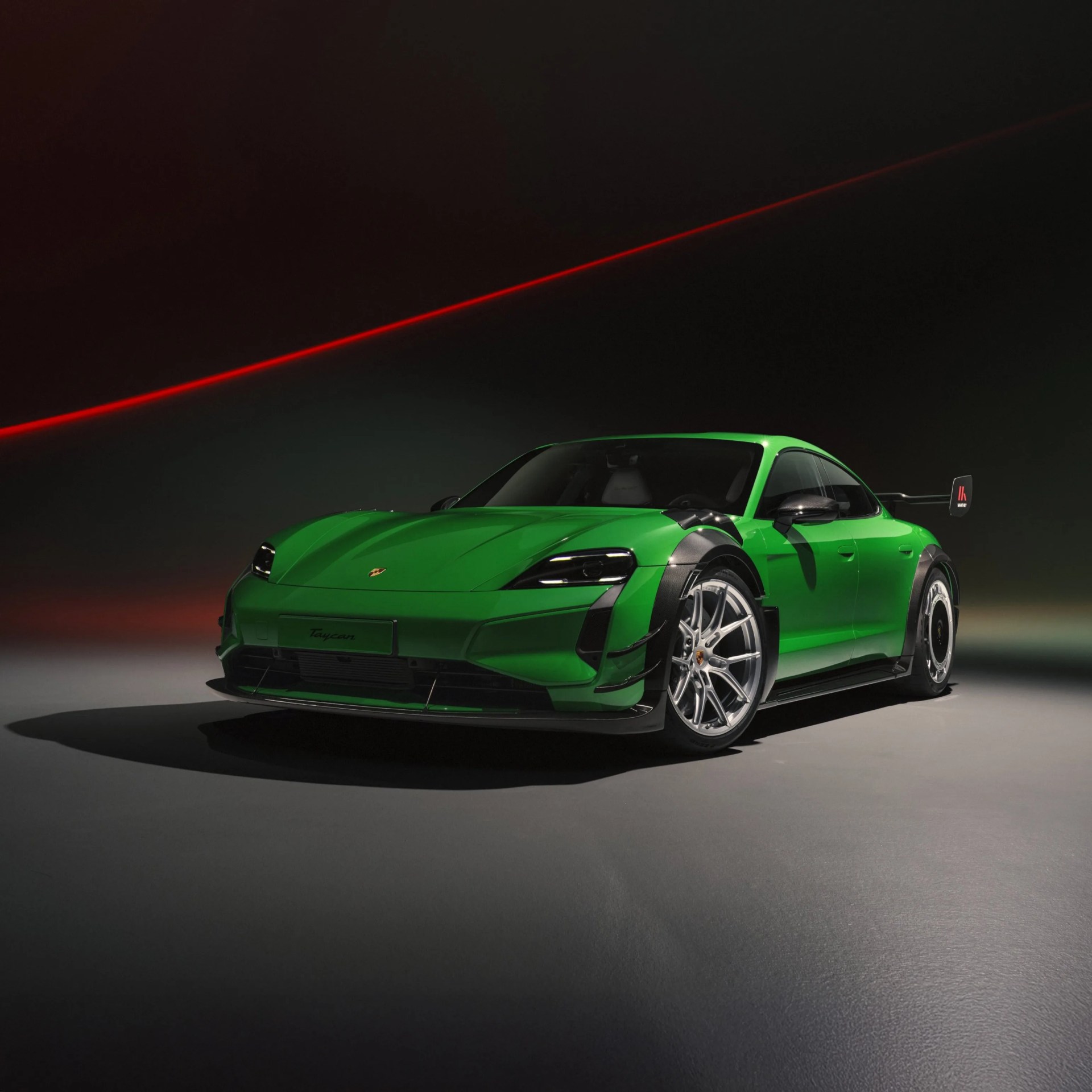 Bright green Porsche Taycan with black carbon fiber accents and a rear wing under a dark sky with a red laser line.