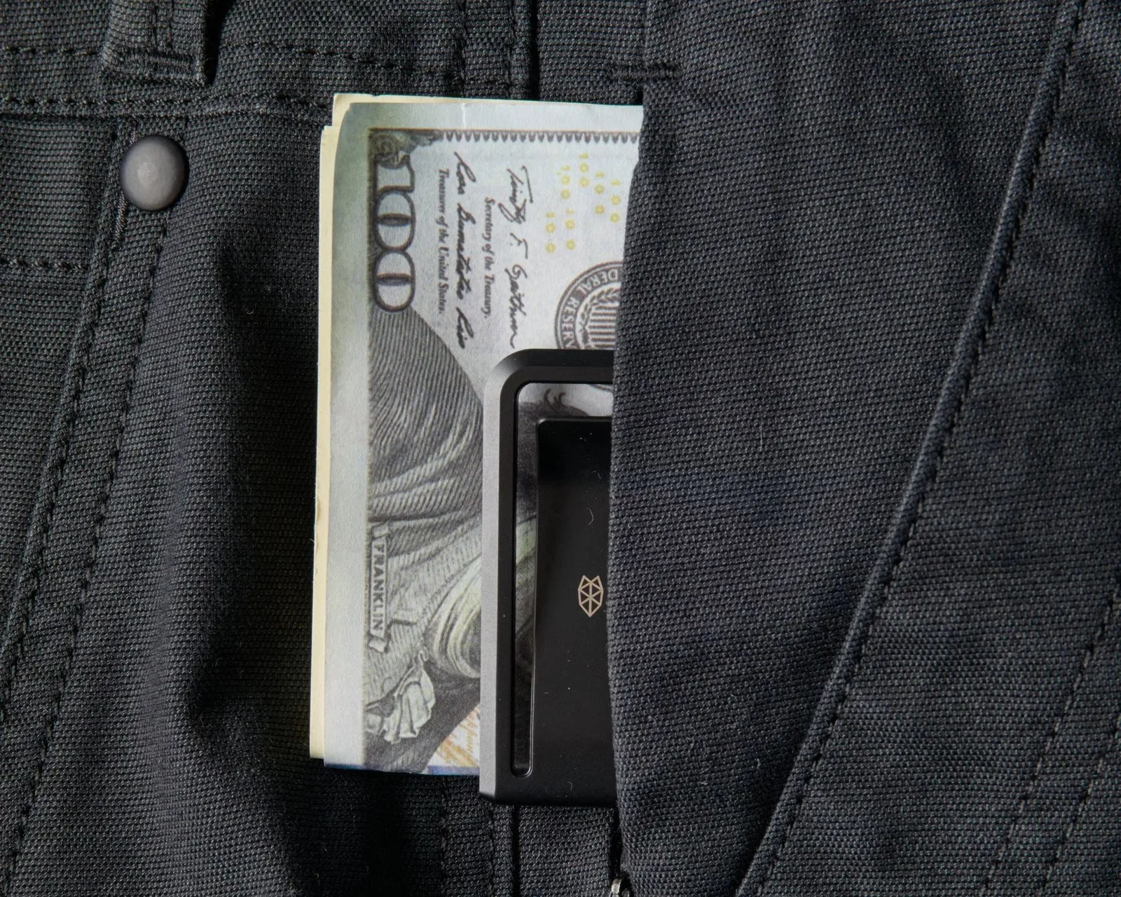 Folded US $100 bill and black cardholder partially visible in a black fabric pocket.