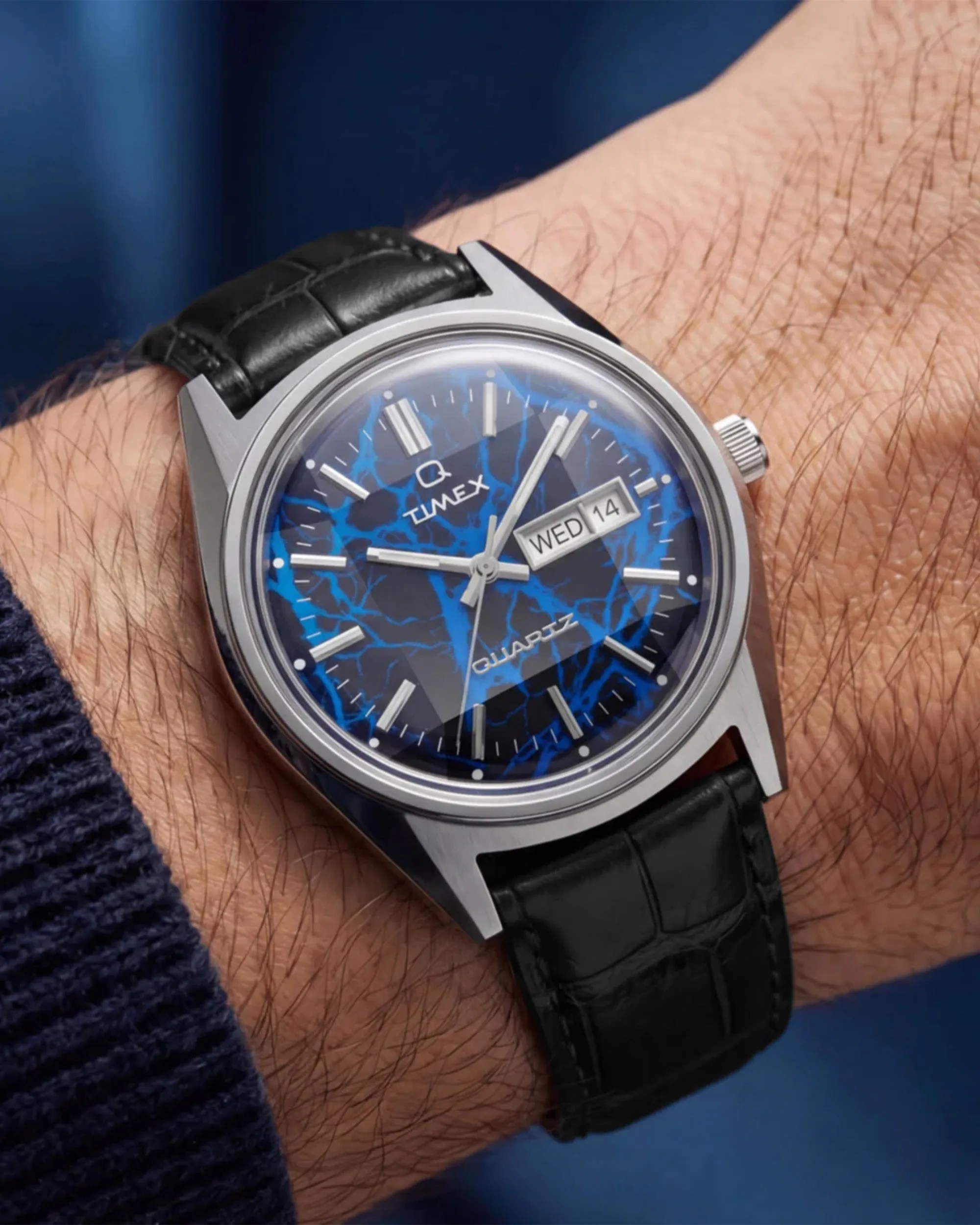 Timex wristwatch with a blue marbled dial, silver markers, day-date display, and black leather strap on a wrist.