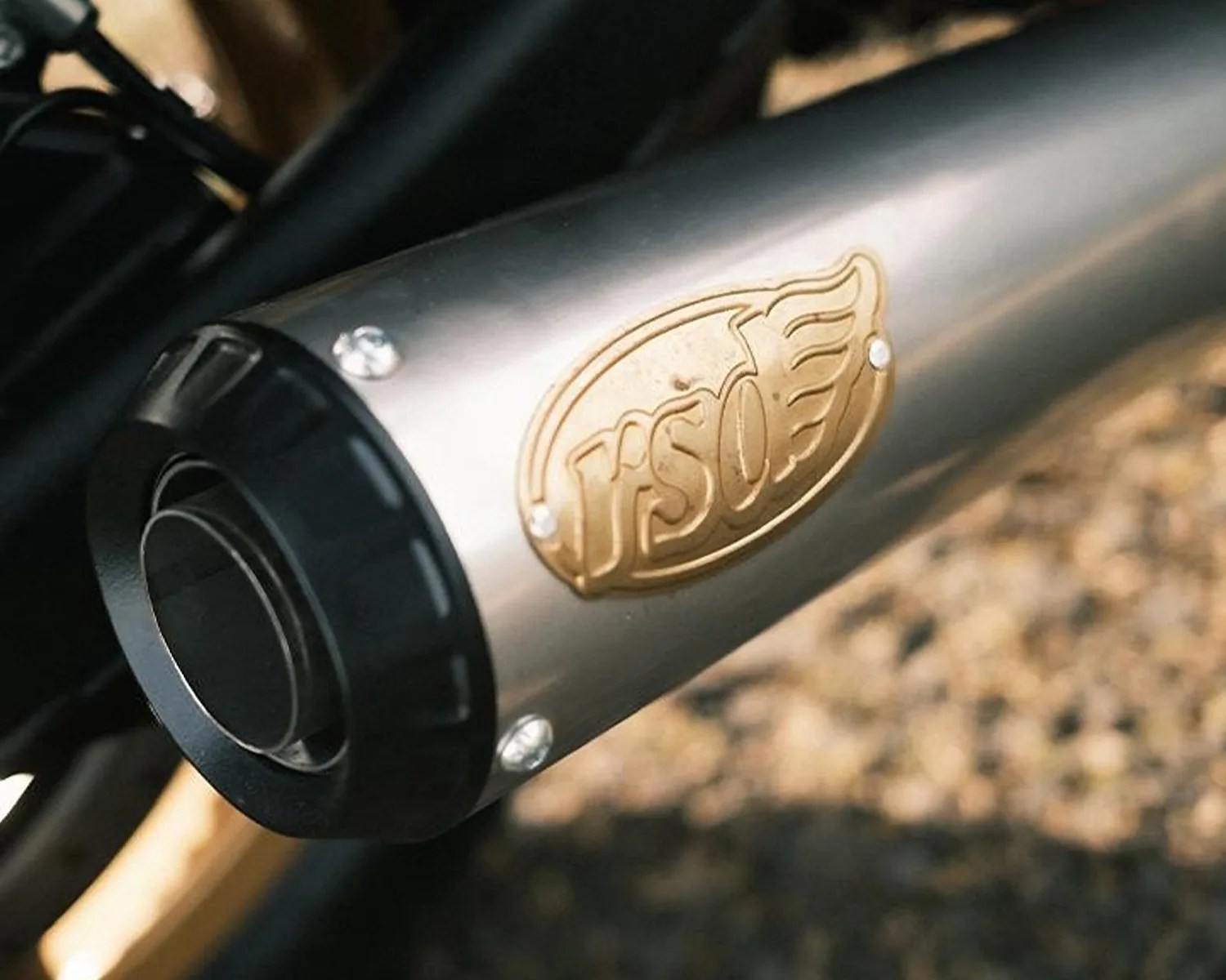 Close-up of a silver motorcycle exhaust pipe with a gold "TSO" emblem and black end cap.