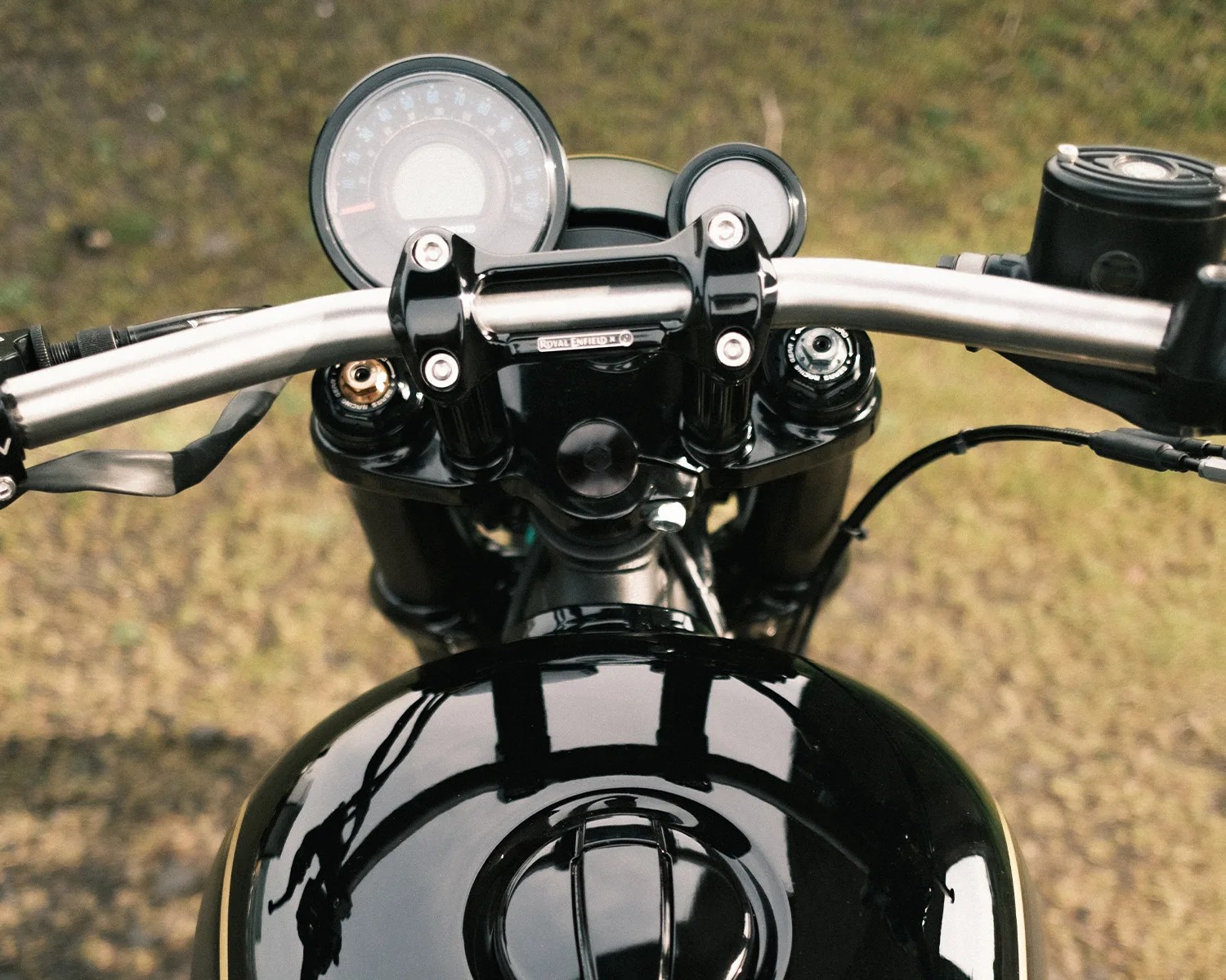 Close-up of a black Royal Enfield motorcycle handlebar and speedometer with a glossy fuel tank below.