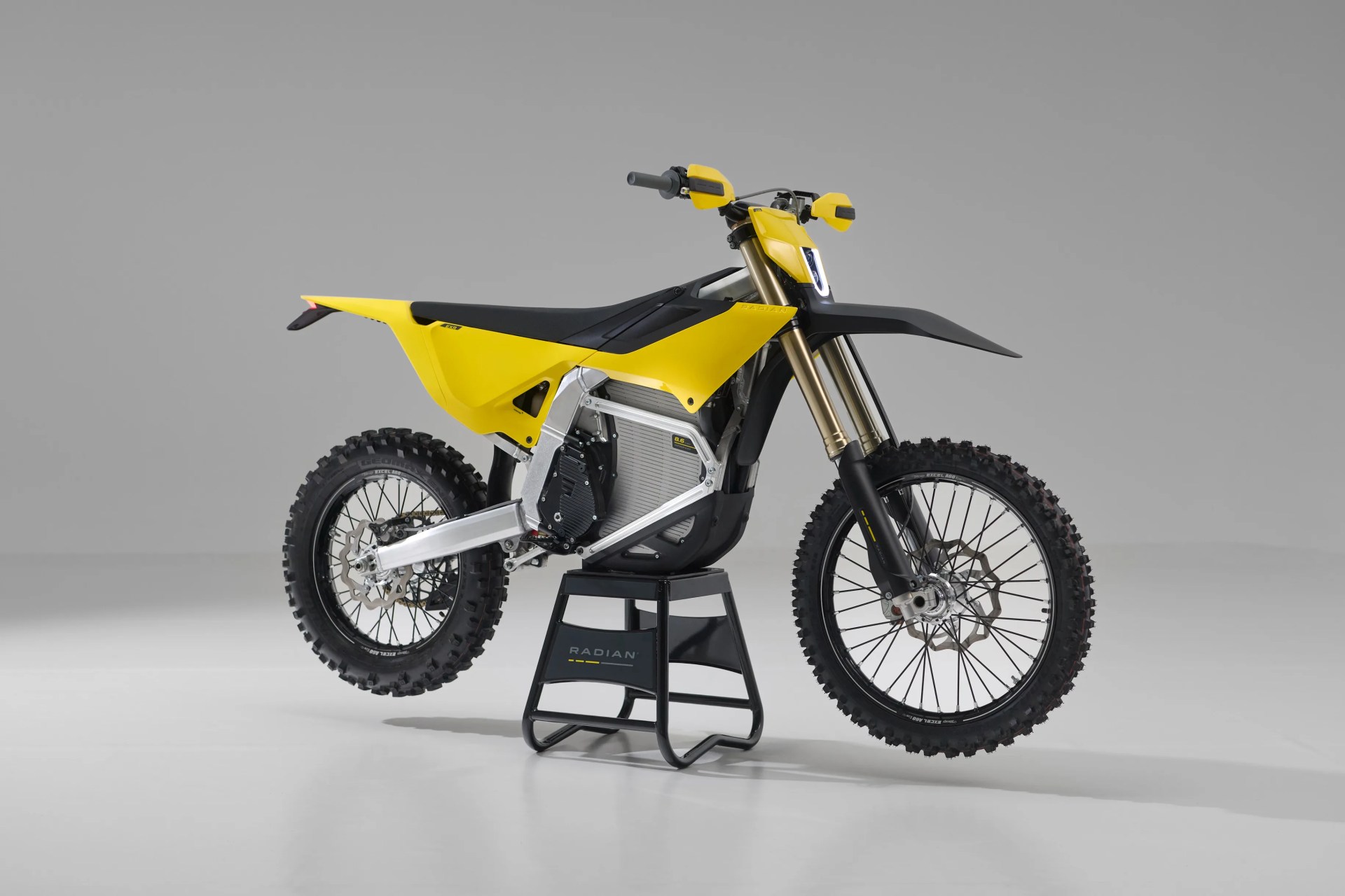 Yellow and black electric dirt bike on a black stand with knobby tires and front suspension forks.