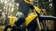 Close-up of a person wearing black gear sitting on a yellow Radian dirt bike in a forest.