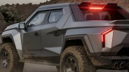 Matte gray off-road truck with angular design and illuminated red rear lights on a dirt road.