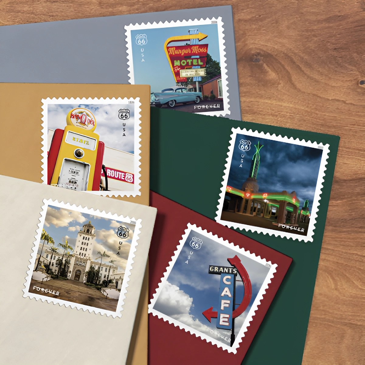Five colorful postage stamps featuring vintage Route 66 signs and buildings on envelopes arranged on a wooden surface.