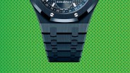 Blue metal watch bracelet with brushed finish and visible screws on a green polka dot background.