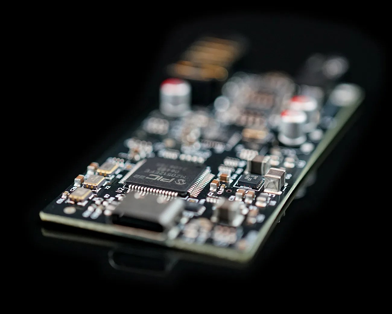 Close-up of a black circuit board with various electronic components and a microchip on a reflective black surface.