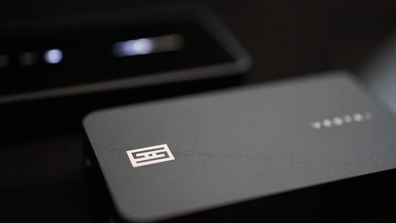 Close-up of a matte black rectangular device with a white geometric logo and blurred text on the surface.