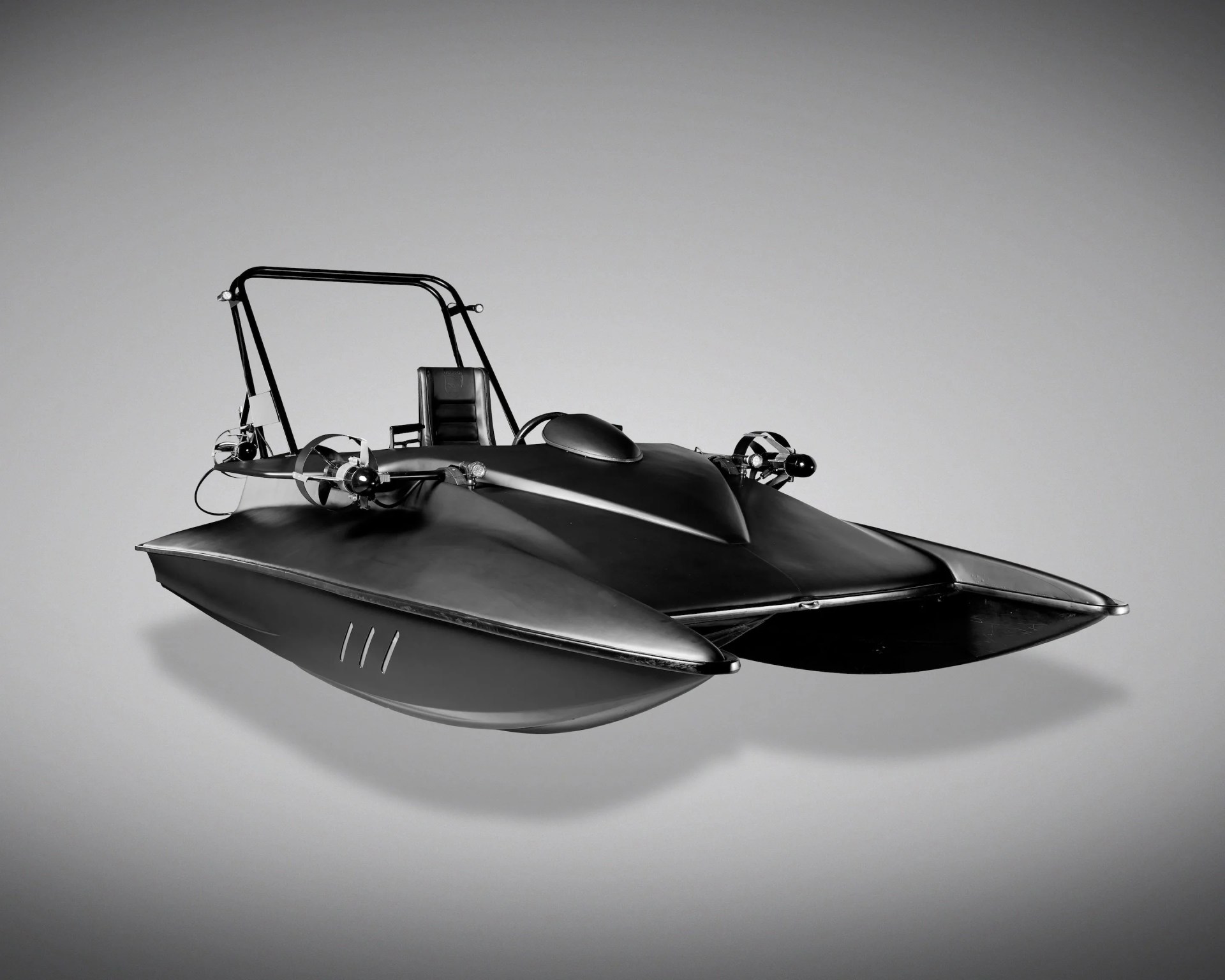 Black vintage hovercraft with a single seat and propellers on each side against a gray background.