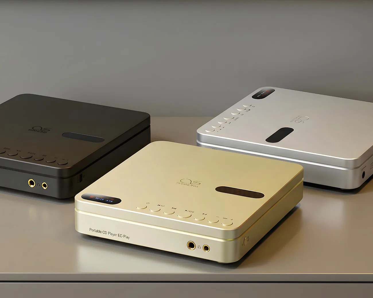 Three square portable CD players in black, gold, and silver with buttons and headphone jacks on a gray surface.