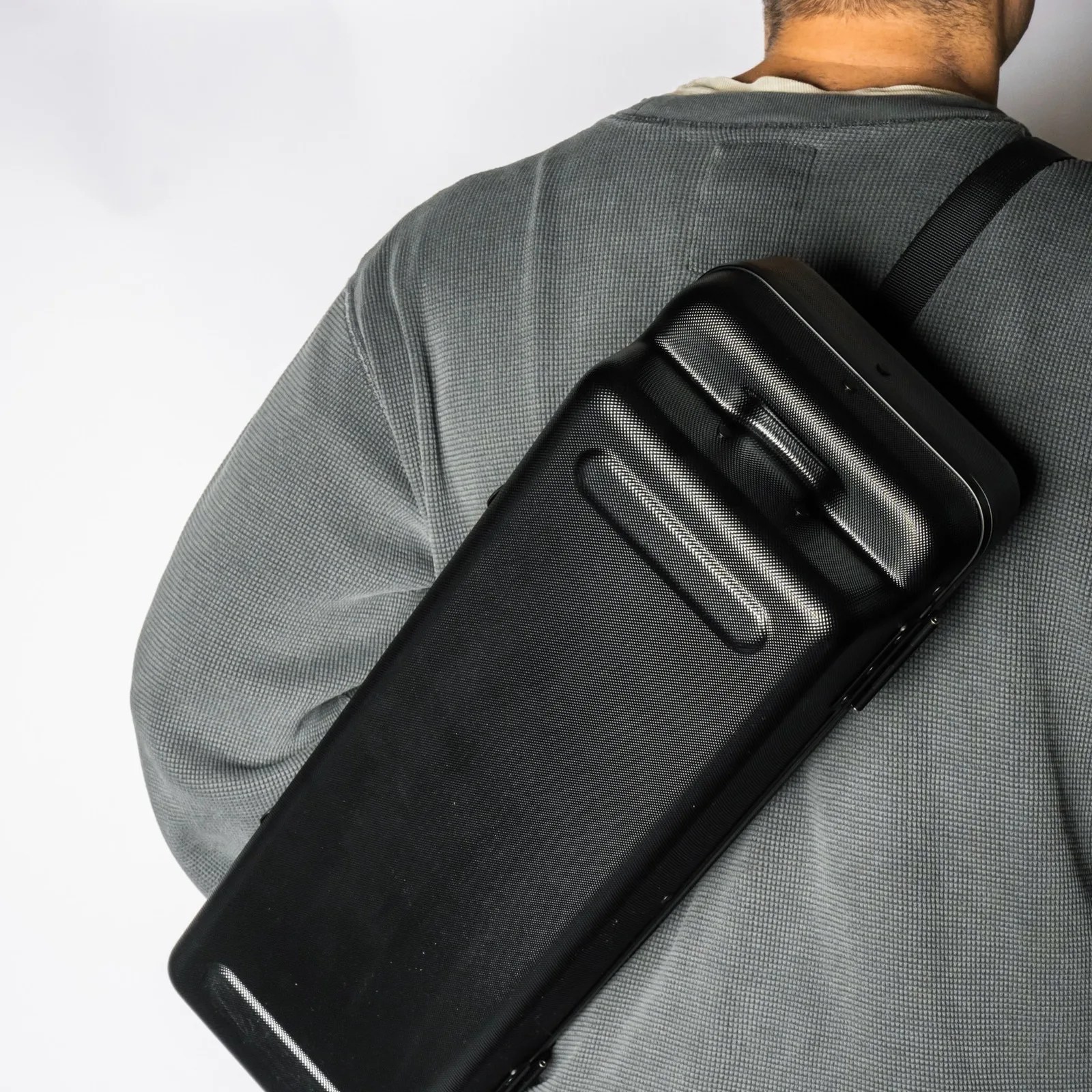 Black textured hard-shell case with handle worn on a shoulder over a gray waffle-knit shirt.