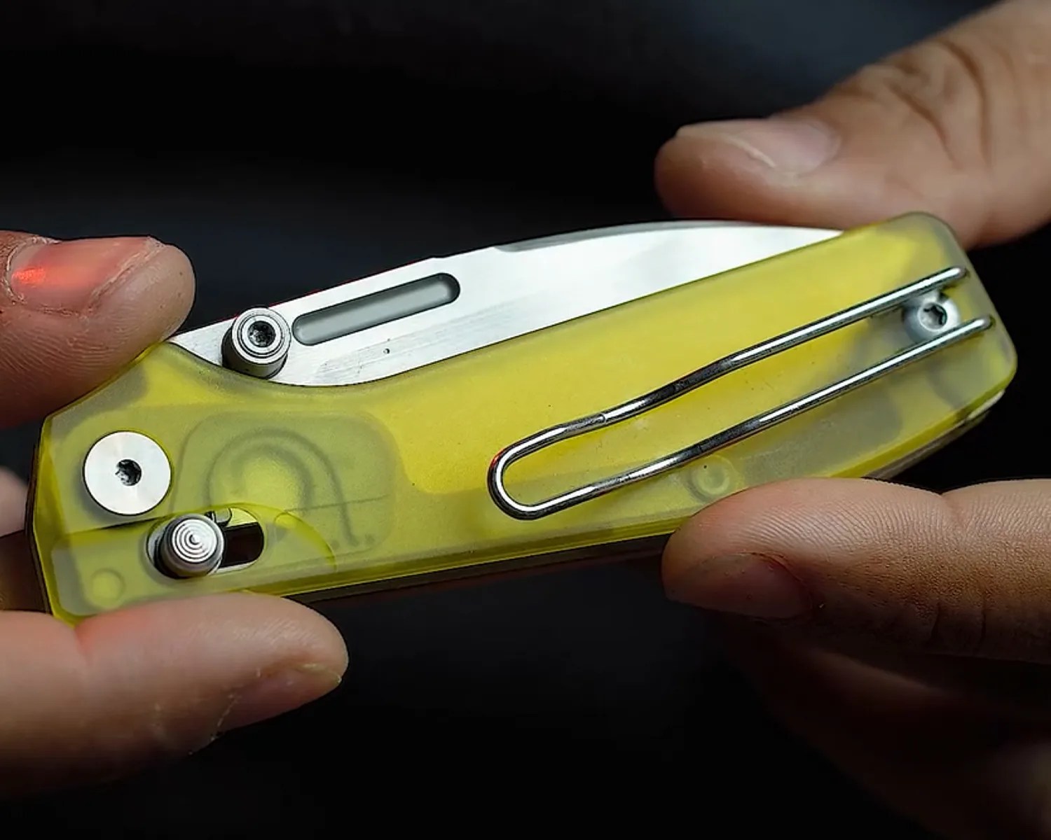 Yellow translucent folding knife with a metal clip held between two hands.