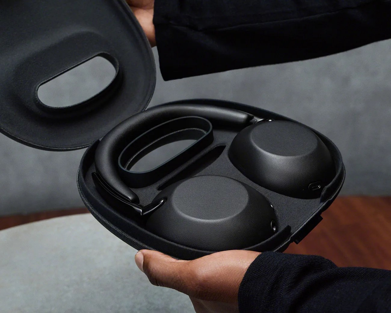 Black over-ear headphones with padded ear cups inside a black hard carrying case held by a person.