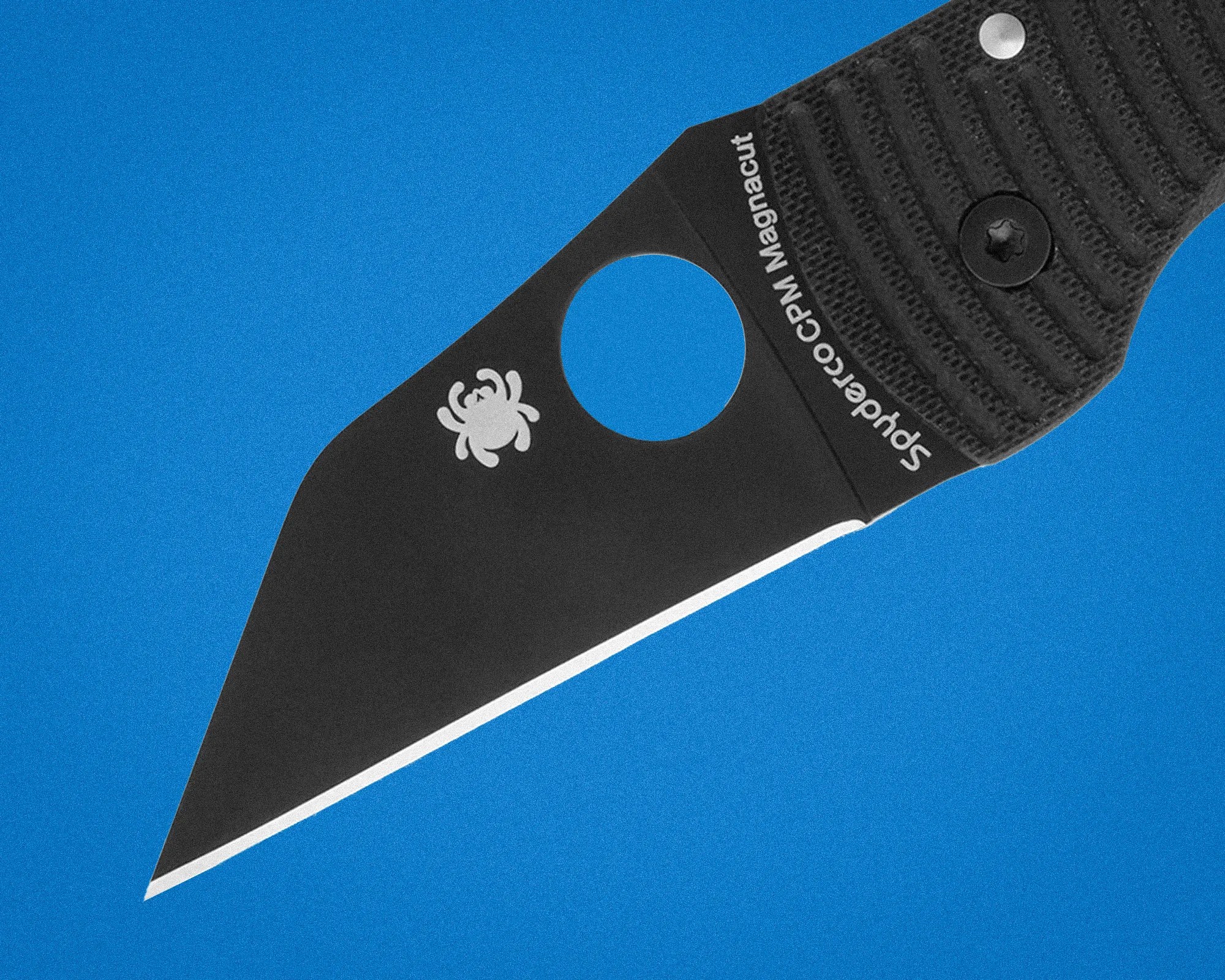 Black Spyderco CPM Magnacut folding knife blade with textured handle on blue background.
