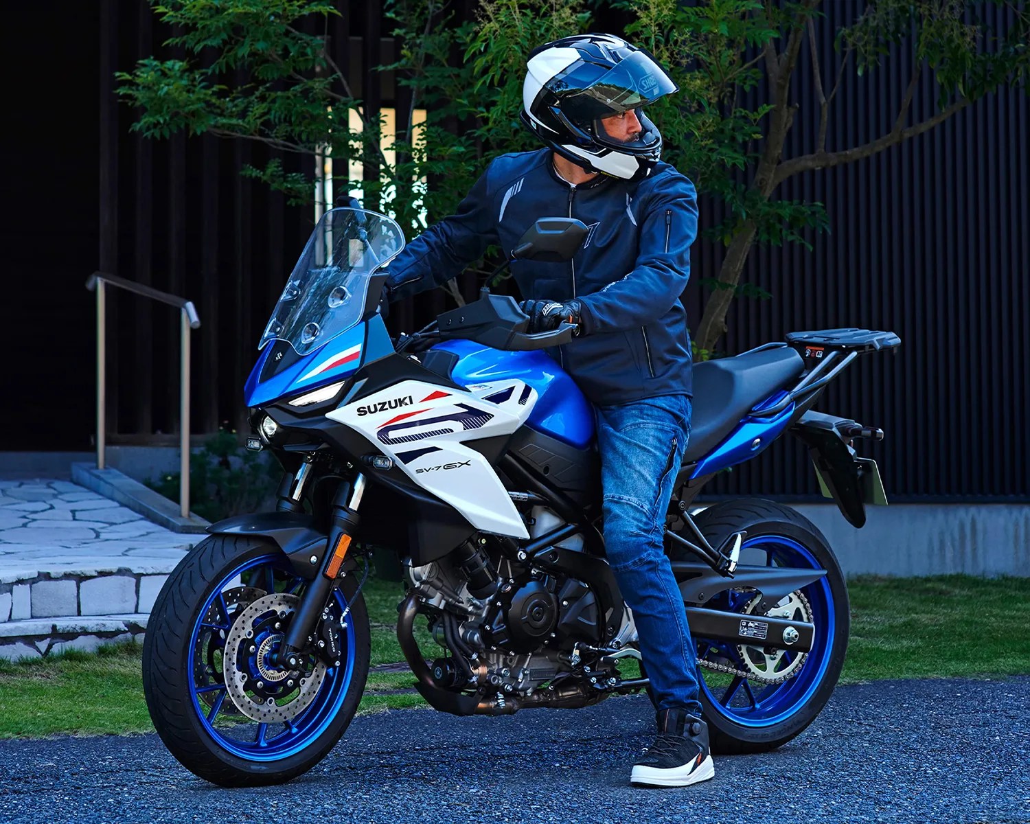 Blue and white Suzuki SV-7 GX motorcycle with blue rims and a rider wearing a black and white helmet and dark jacket.