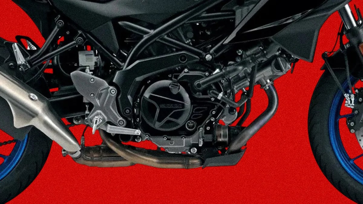 Close-up of a black motorcycle engine and exhaust system with blue wheels against a red background.