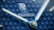 Close-up of blue textured watch face with white "AP x Swatch" logo and light blue hour and minute hands.