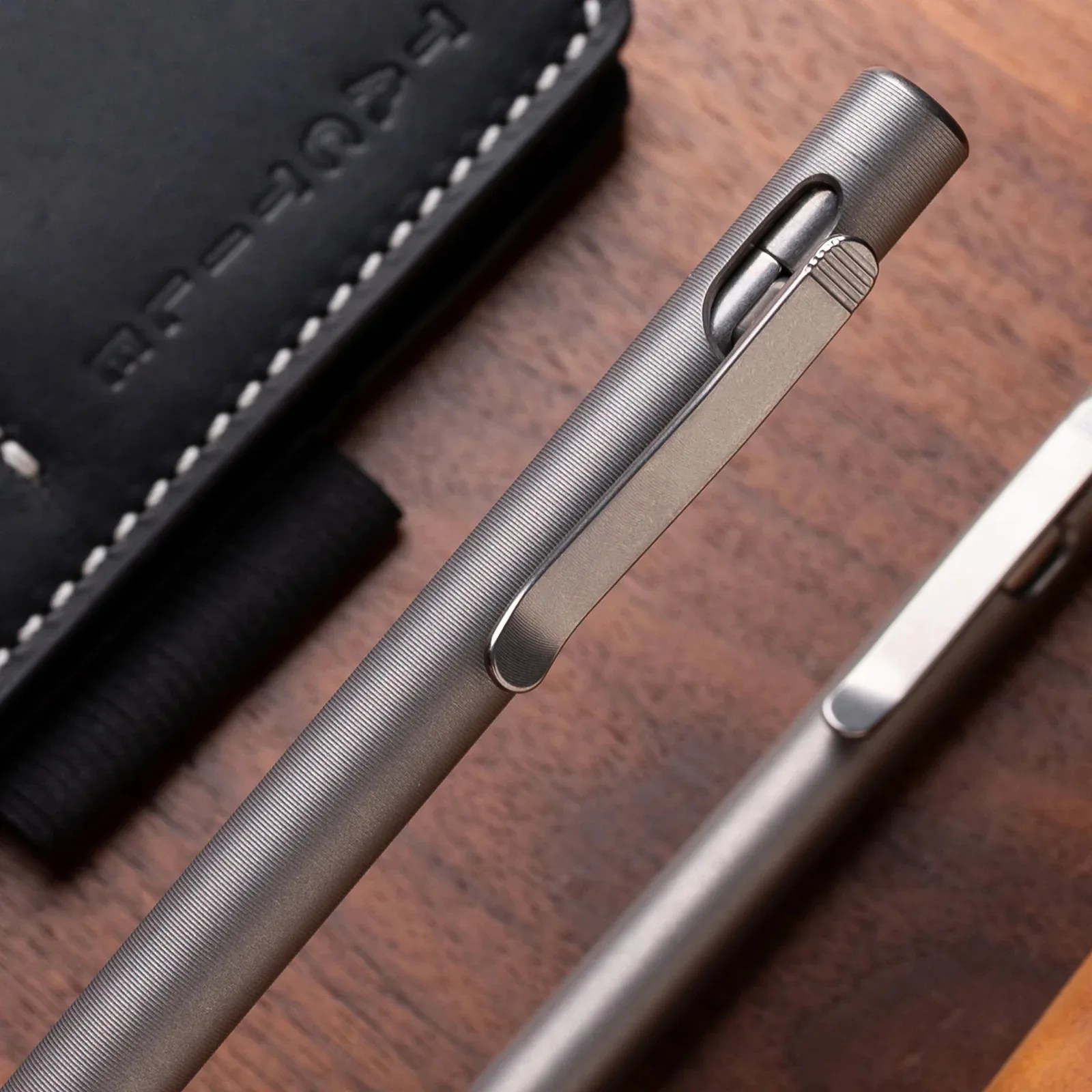 Close-up of a textured silver metal pen with a clip on a wooden surface next to a black leather case.
