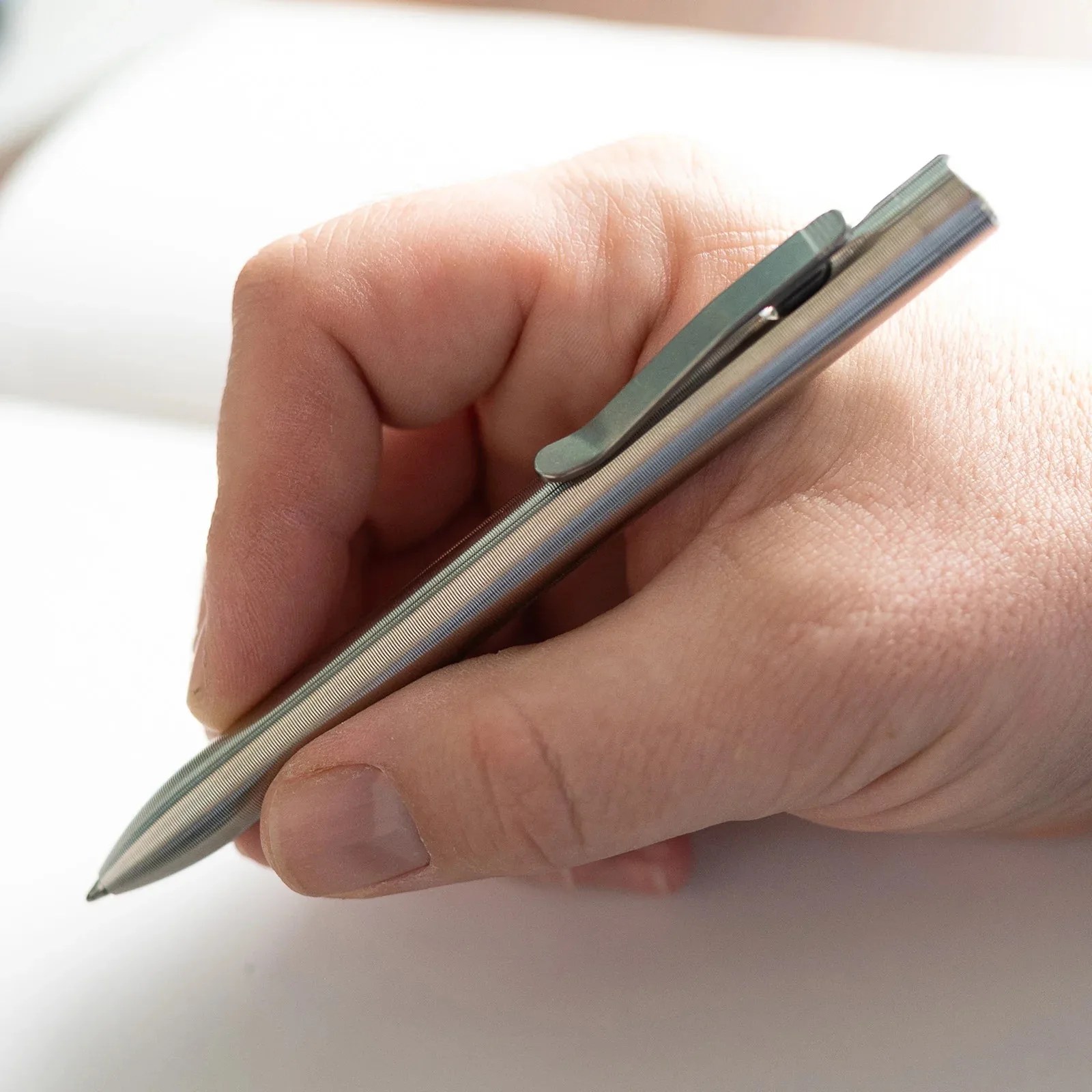 Hand holding a silver metal pen with a clip over a white surface.