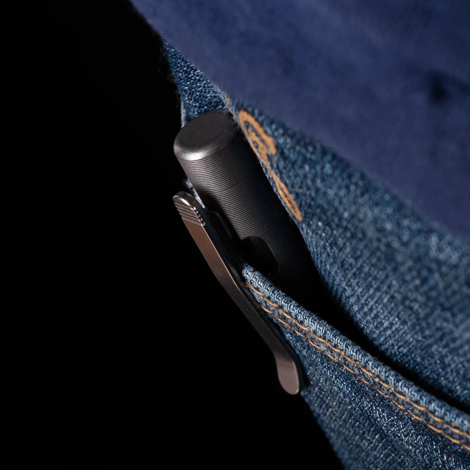 Black textured pen clipped to the edge of a blue denim pocket with orange stitching.