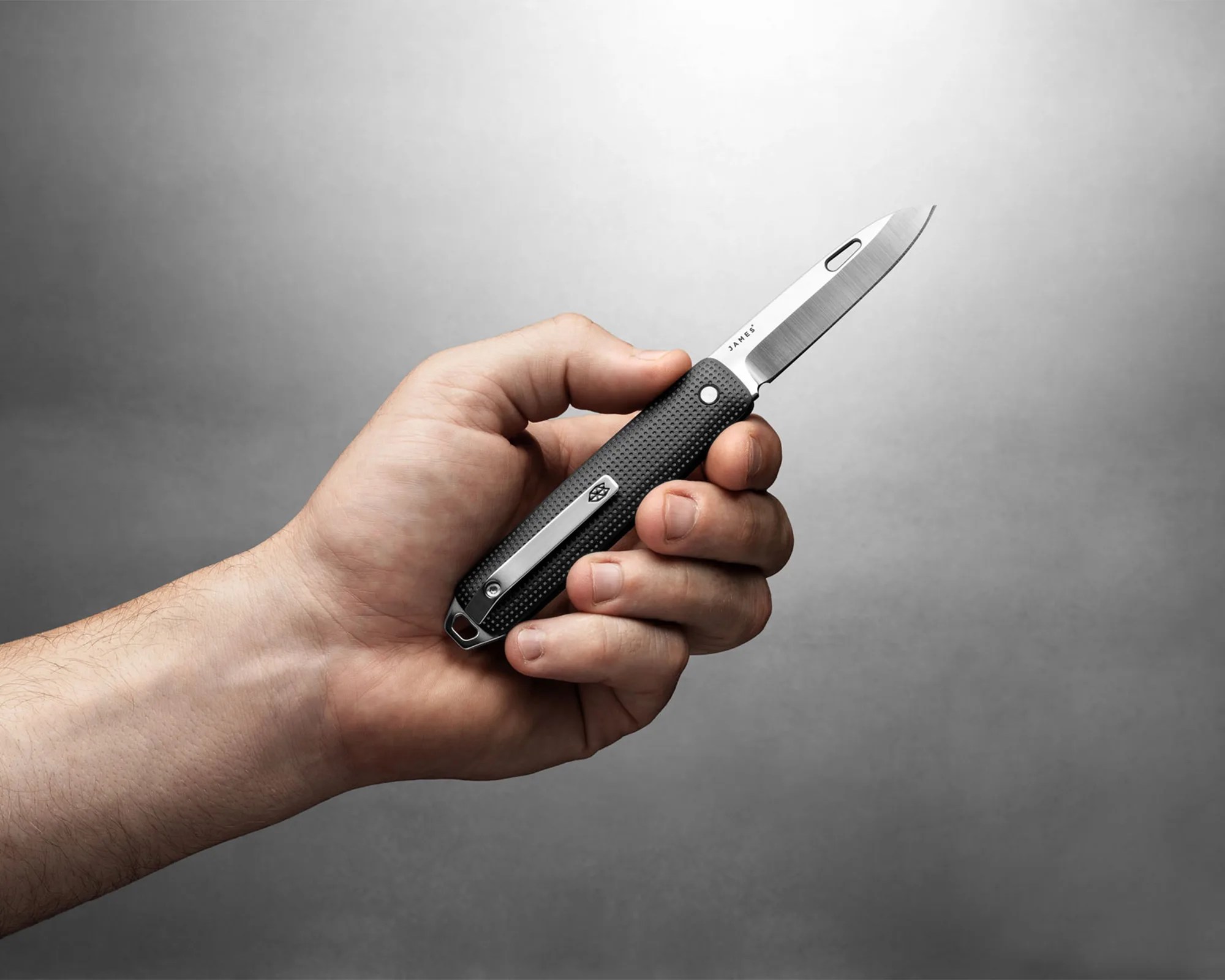 Hand holding a black textured folding knife with a partially serrated stainless steel blade.