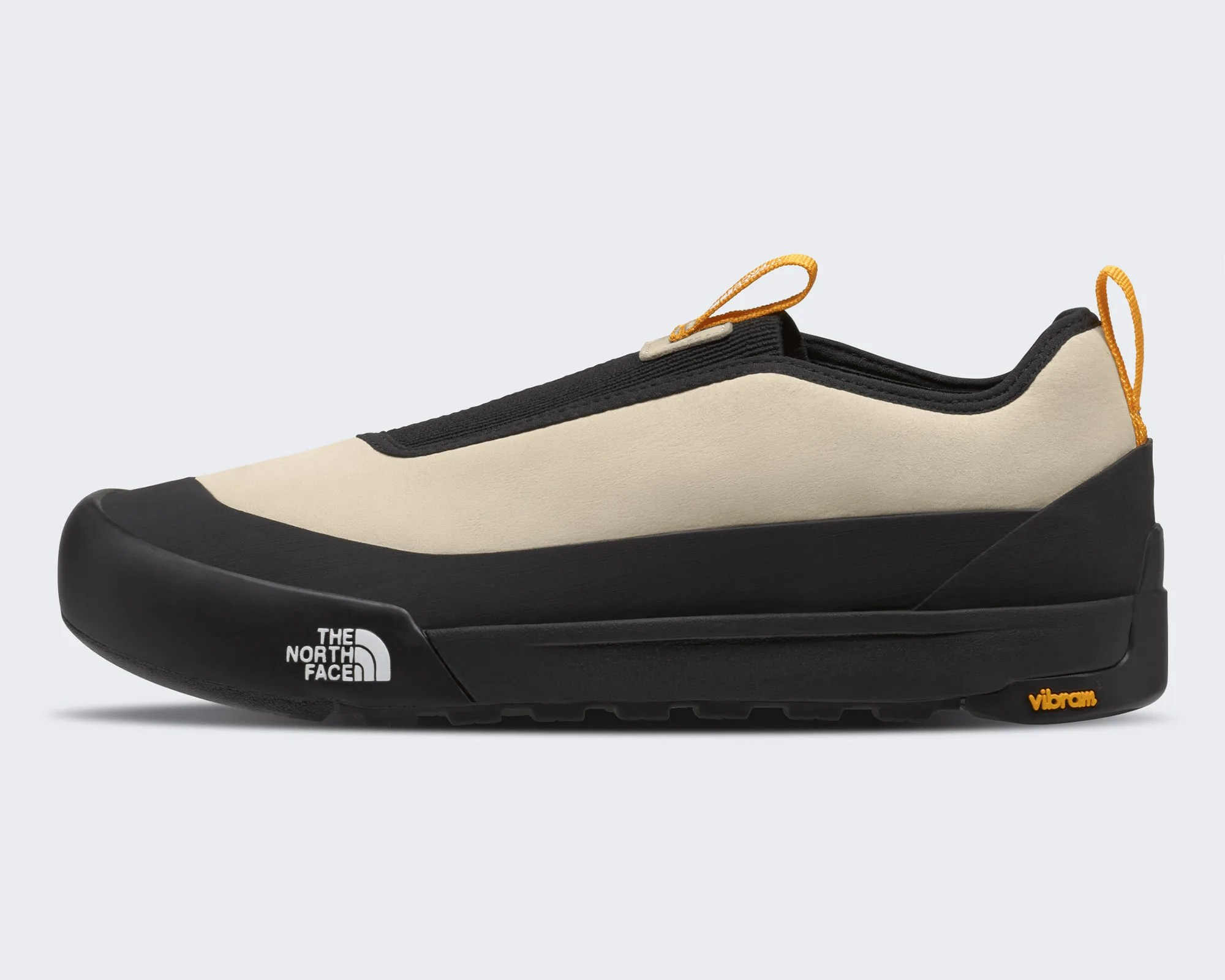 Beige and black slip-on shoe with orange pull tabs, The North Face logo on the sole, and Vibram branding.