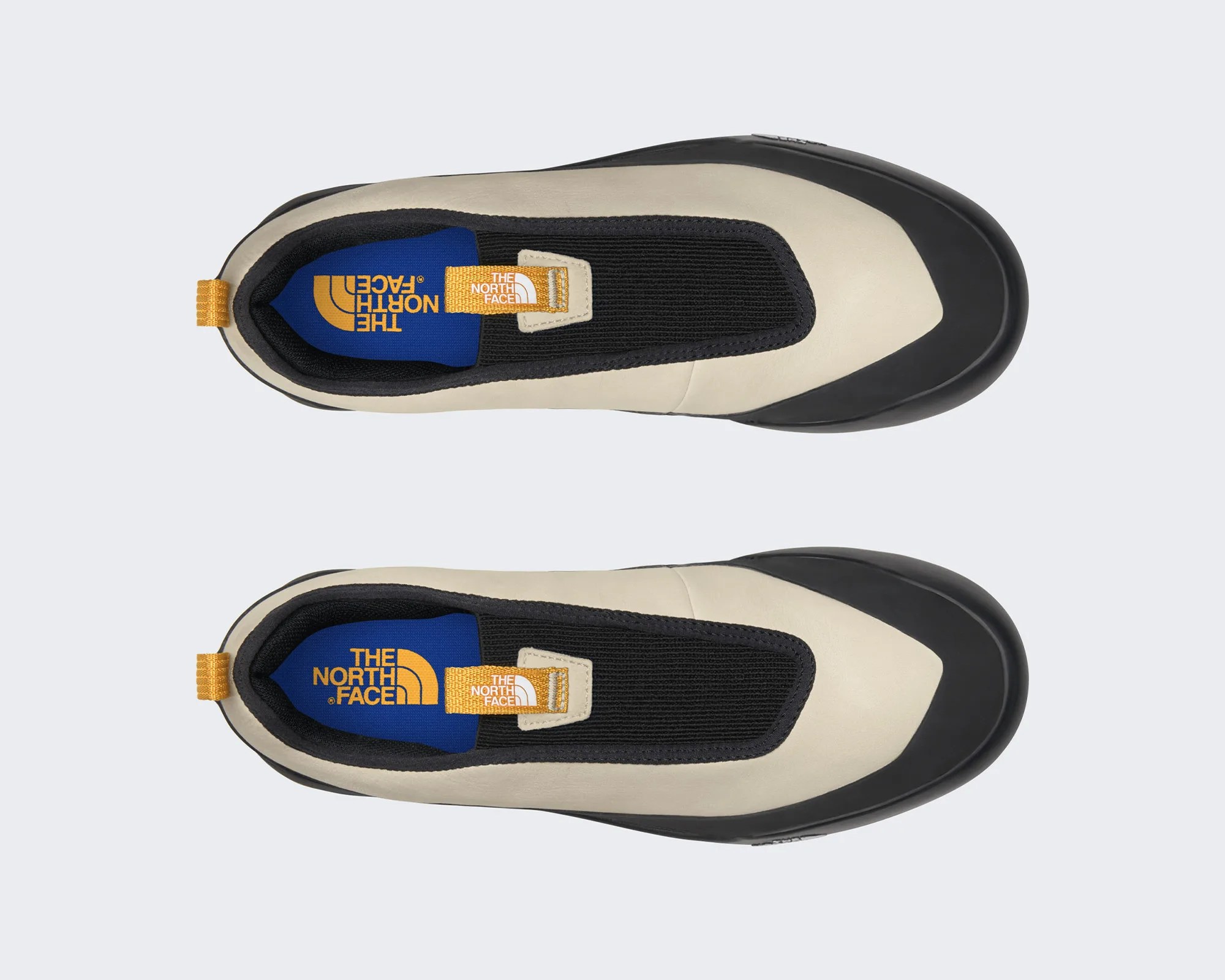 Beige and black slip-on shoe with blue insole and yellow pull tab featuring The North Face logo.
