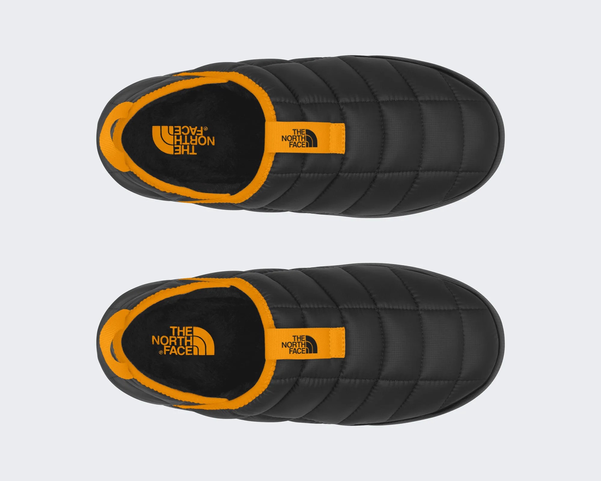 Black quilted slip-on shoe with orange trim and The North Face logo on the insole and pull tab.