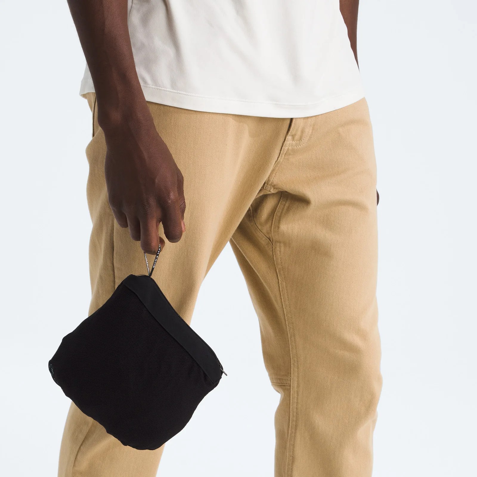 Hand holding a small black zippered pouch against tan pants and a white shirt.