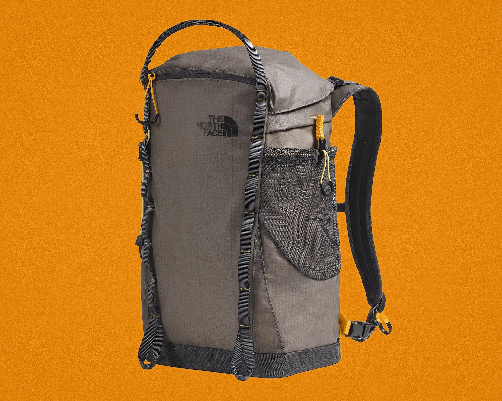 Gray The North Face backpack with black straps and yellow zipper pulls against an orange background.