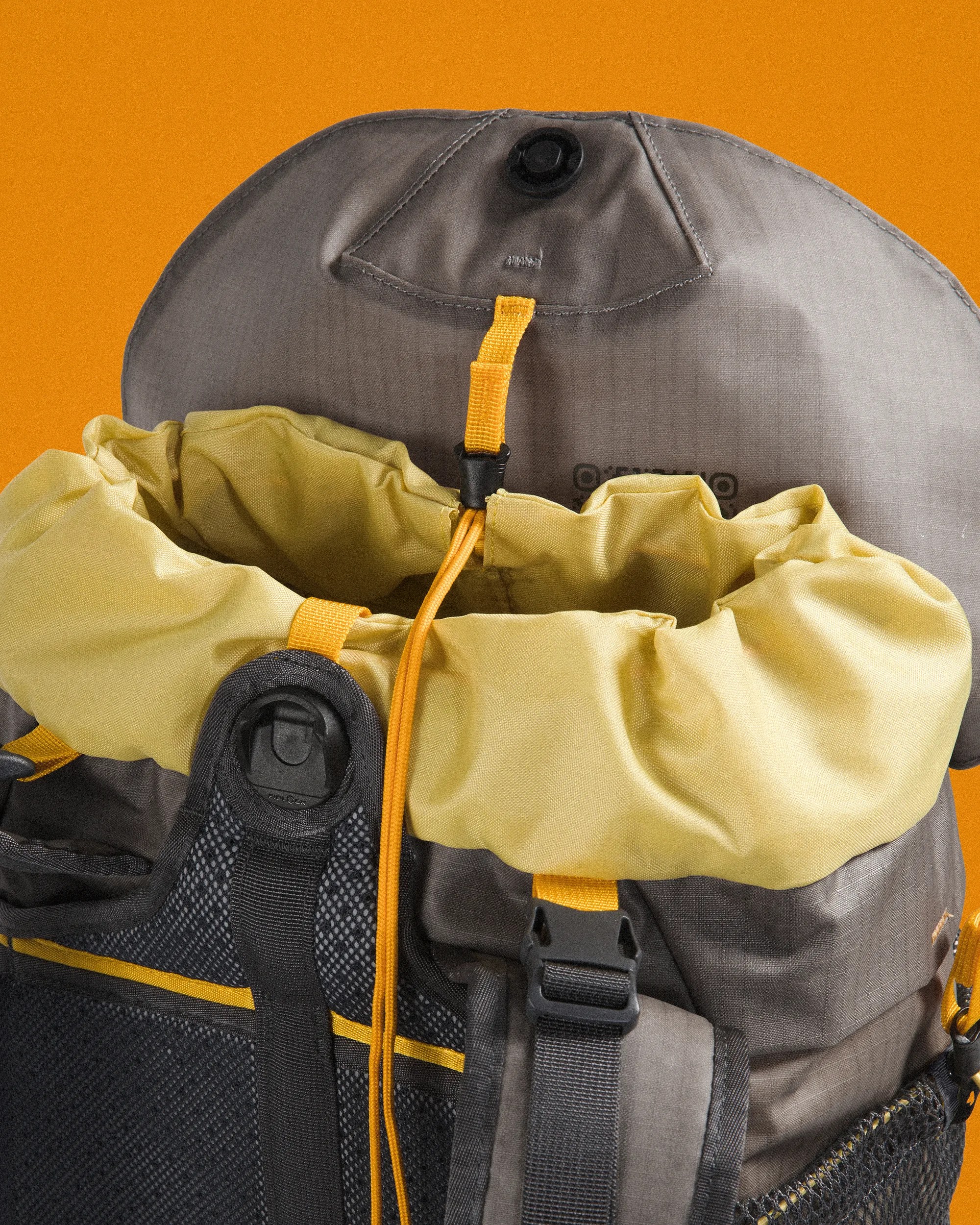 Close-up of a gray and yellow backpack top with drawstring closure and black buckle on an orange background.