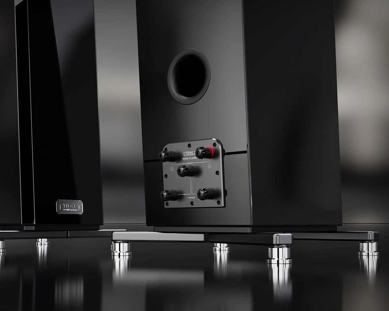 Glossy black Tidal Piano Classic speaker with rear bass port and connection terminals on a reflective surface.