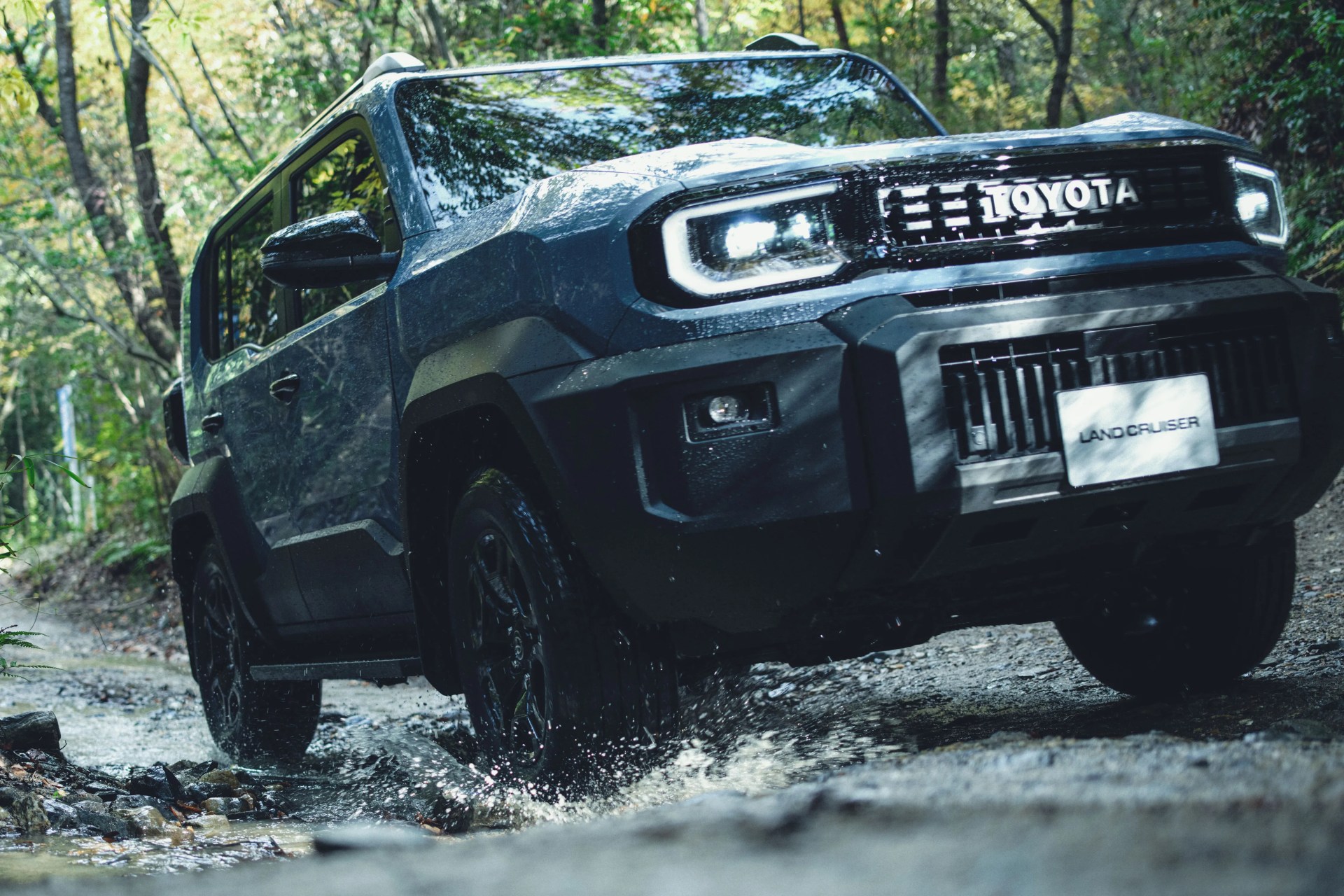 Dark blue Toyota Land Cruiser driving through a shallow rocky stream in a forest.