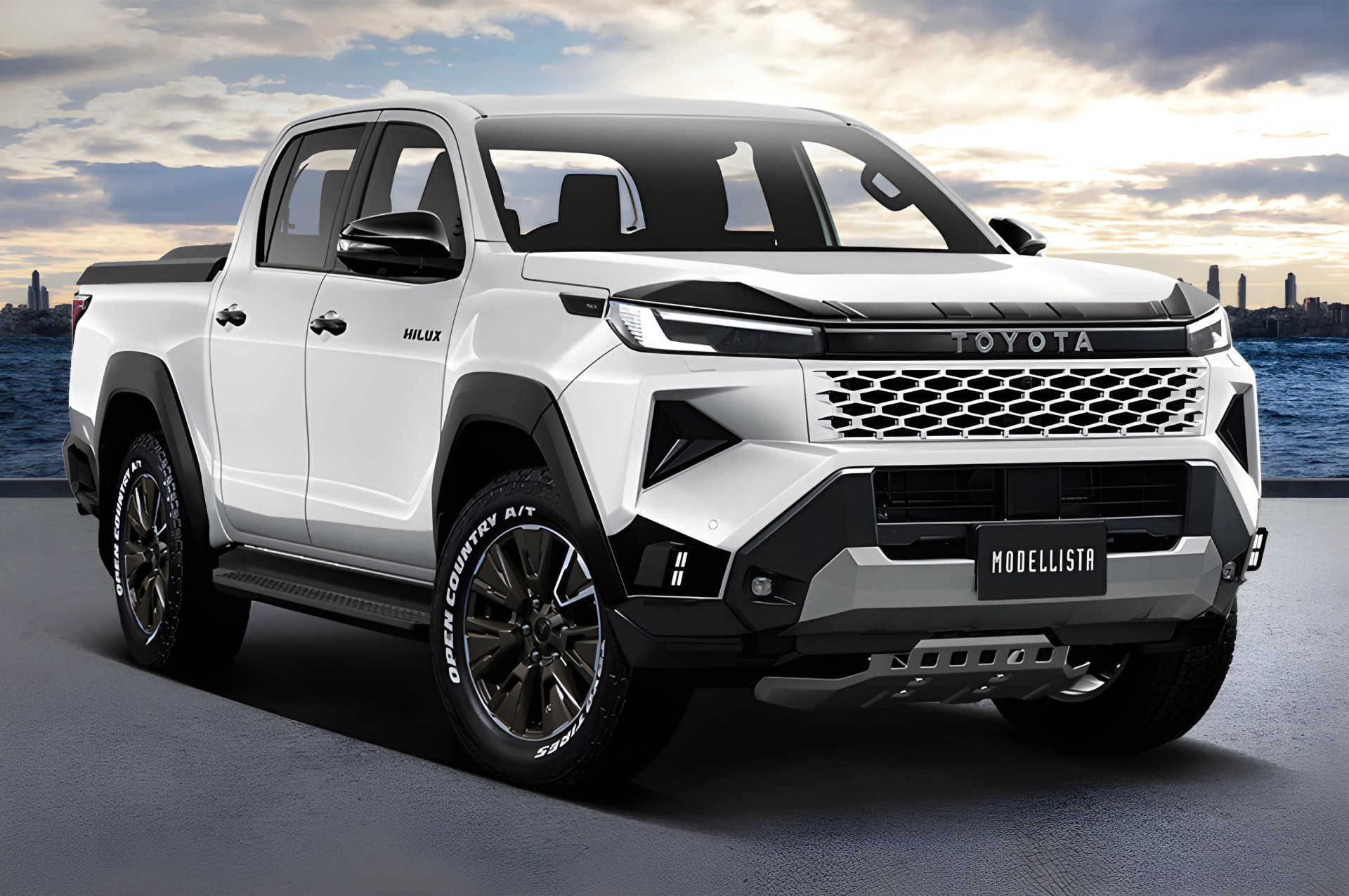 White Toyota Hilux pickup truck with black accents and Modellista badge parked near water at sunset.