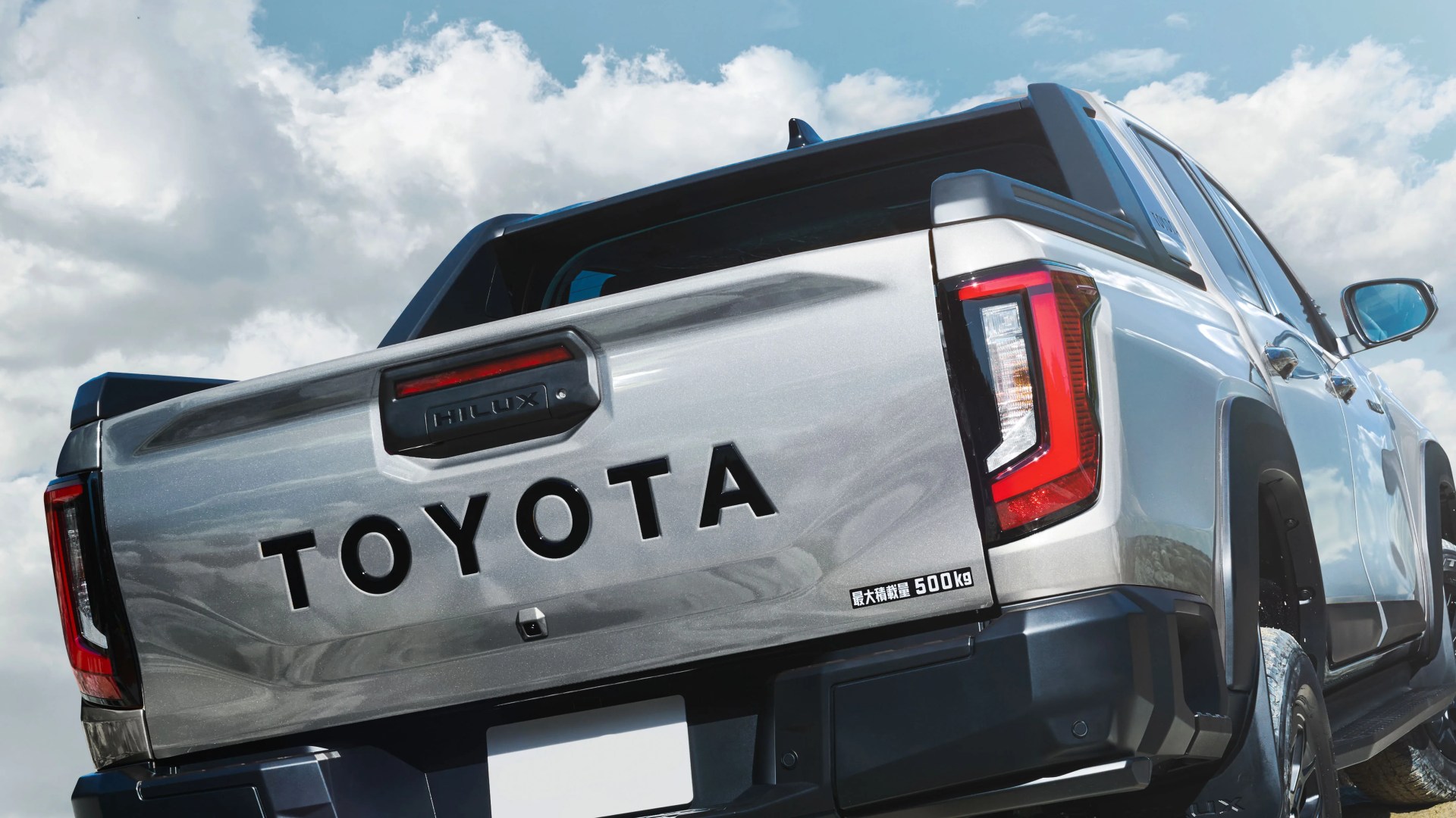 Silver Toyota Hilux pickup truck bed with black trim and red-accented taillights under a partly cloudy sky.