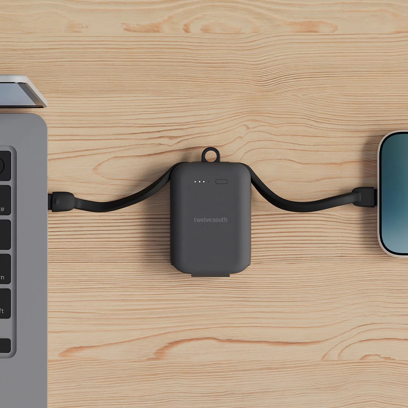 Black Twelve South charging case connected between a laptop and wireless earbuds on a wooden surface.