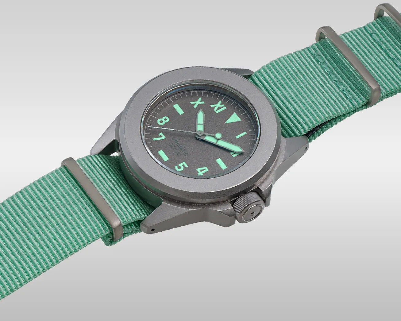 Matte gray wristwatch with luminescent green hands and markers on a mint green nylon strap.