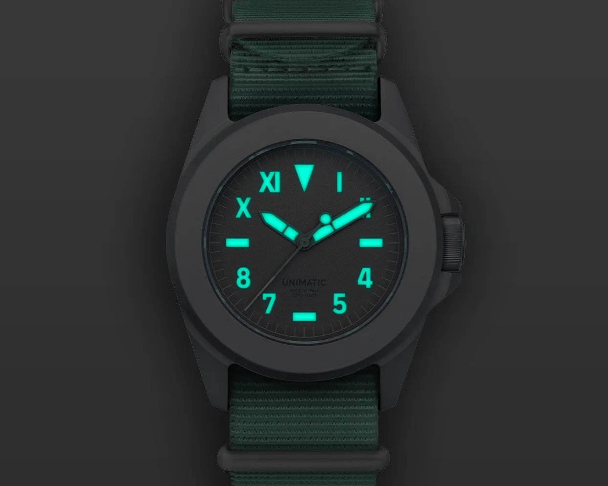 Black matte wristwatch with glowing turquoise hands and numerals on a dark green nylon strap.