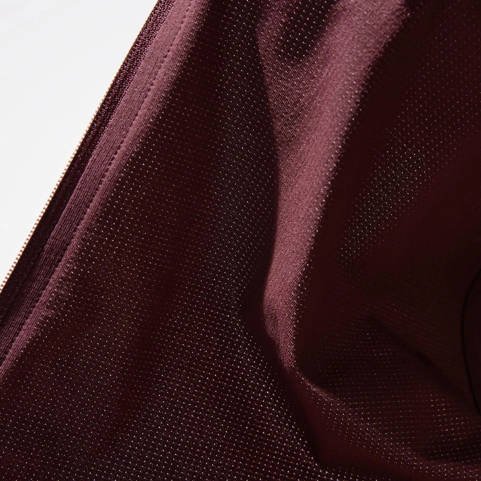 Close-up of maroon fabric with a fine dotted texture and visible stitching along the edge.