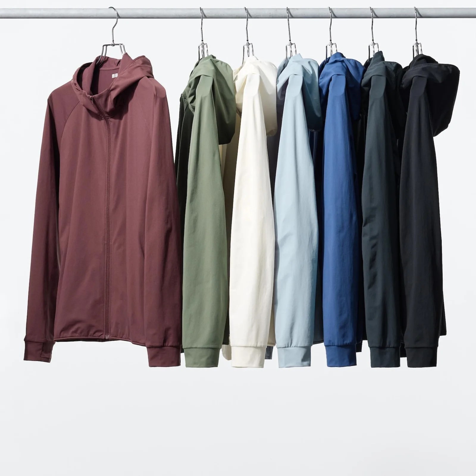 Seven hooded zip-up jackets in burgundy, olive green, off-white, light blue, blue, dark green, and black hanging on a metal rack.
