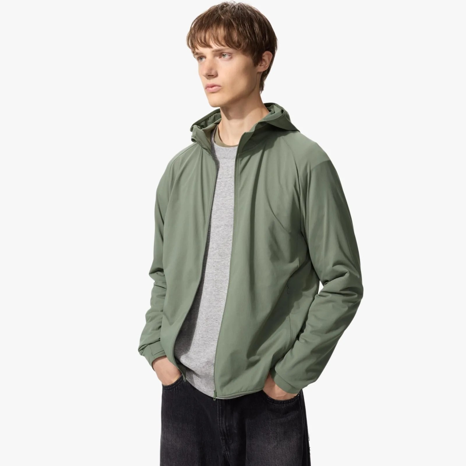Light olive green zip-up jacket with hood worn over a gray shirt and black pants.