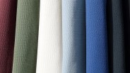 Seven rolls of textured fabric in burgundy, olive green, white, light blue, blue, dark gray, and black colors.