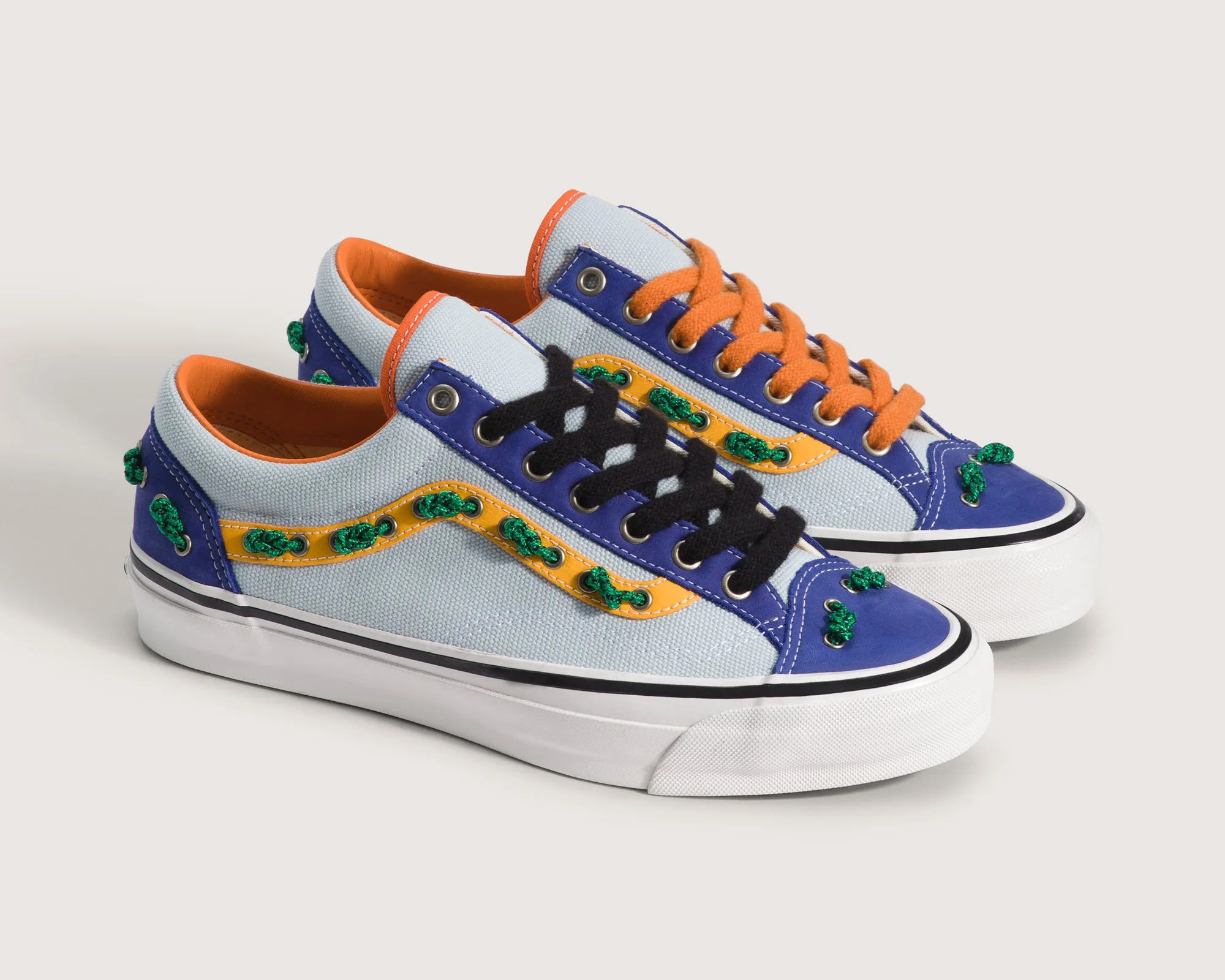 Pair of low-top canvas sneakers with blue, orange, and yellow accents, green embroidered details, and mismatched orange and black laces.