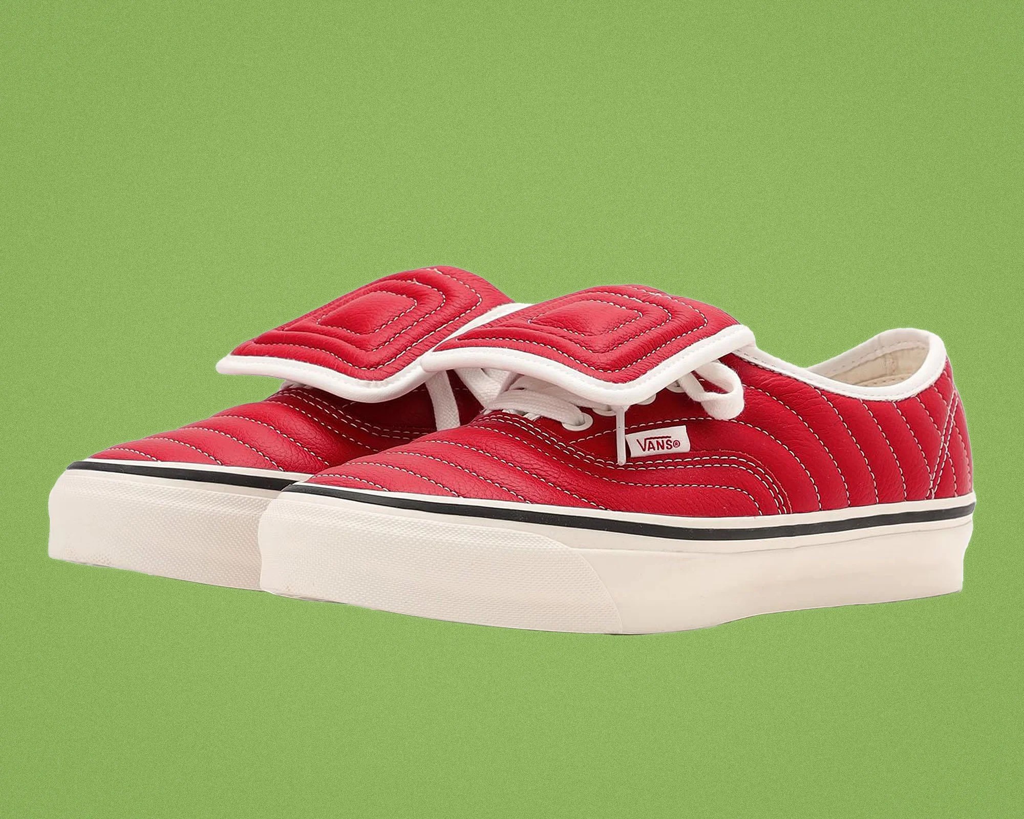 Pair of red Vans sneakers with white stitching, white laces, and thick white soles on green background.