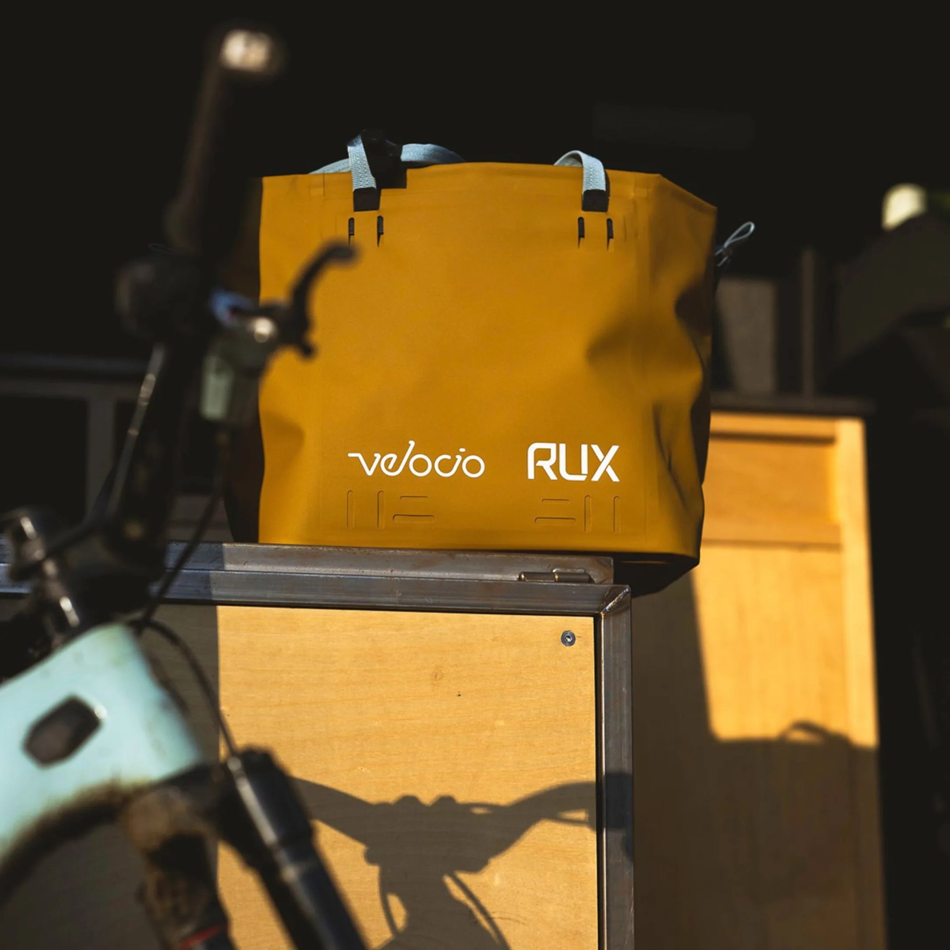 Yellow Velocio RUX bag with light blue handles mounted on a bike rack.